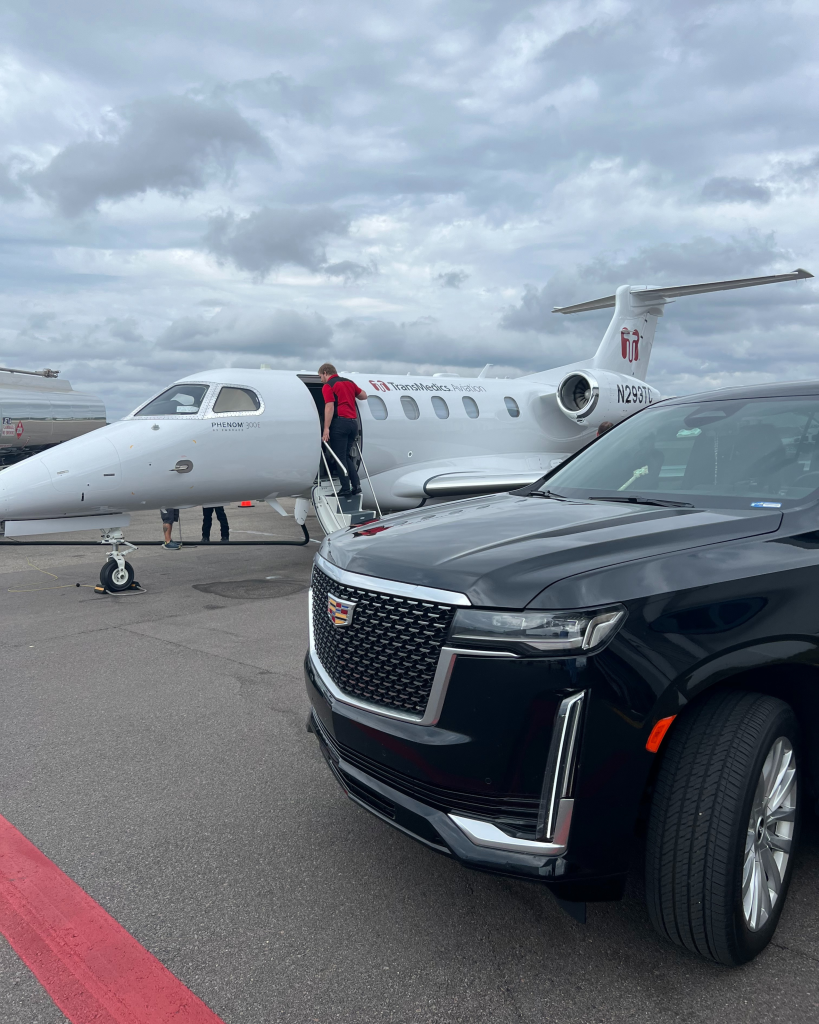 A black luxury SUV parked next to a private jet on a cloudy day, with a person boarding the aircraft.