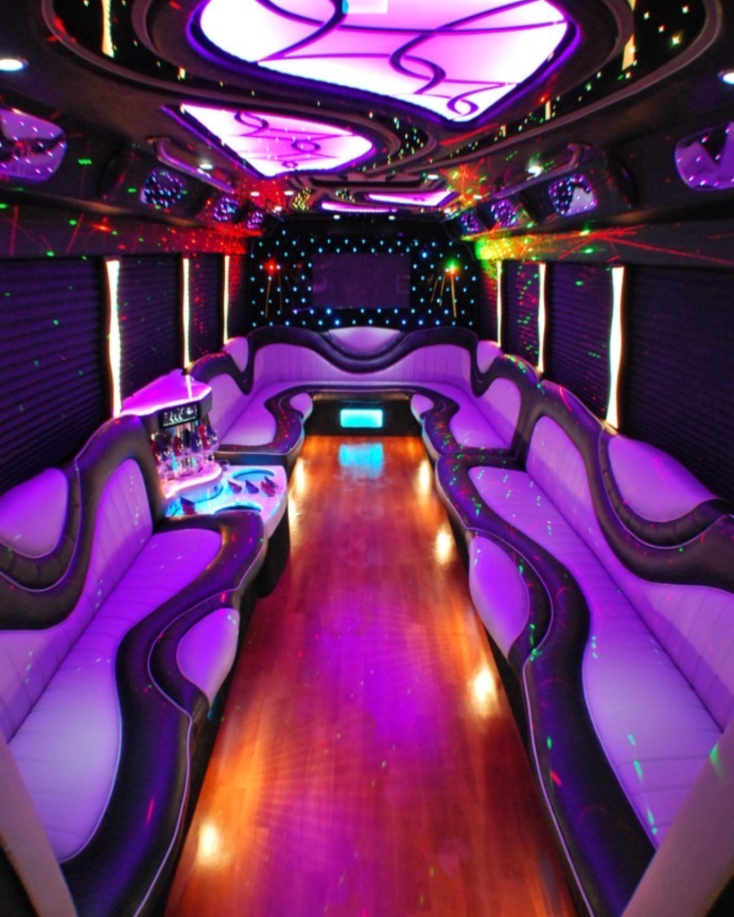 Interior of a party bus featuring vibrant purple lighting, comfortable seating, and a stylish design