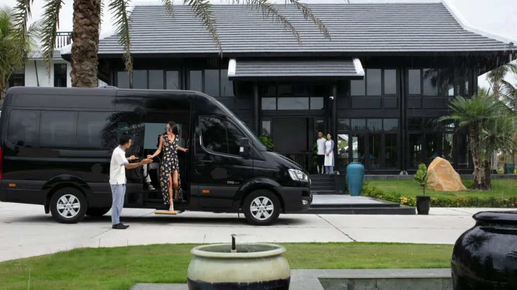 A luxury black van at a modern building entrance, with a chauffeur assisting a woman in a dress as she steps out.